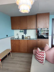In-room kitchenette at room2 Chiswick hometel in London with wooden cabinets, sink, oven, and compact cooking area beside a sofa for flexible long stays