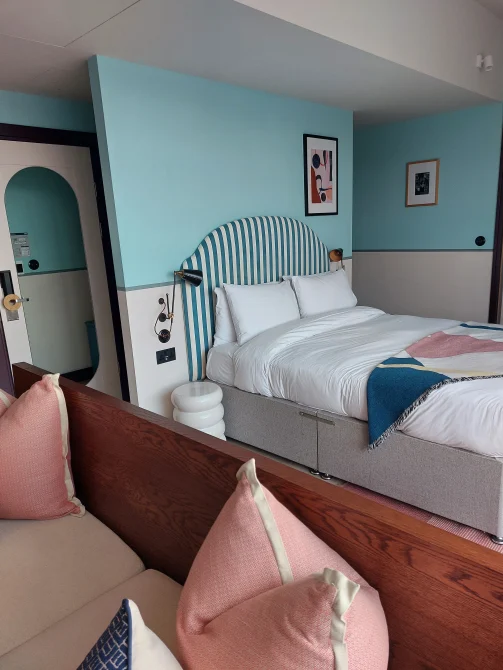 Studio room at room2 Chiswick hometel in London with turquoise accent walls, queen bed with striped headboard, modern furnishings, and compact living space