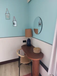 Workspace nook at room2 Chiswick hometel in London with wooden desk, chair, round mirror, turquoise walls, and local handcrafted decor