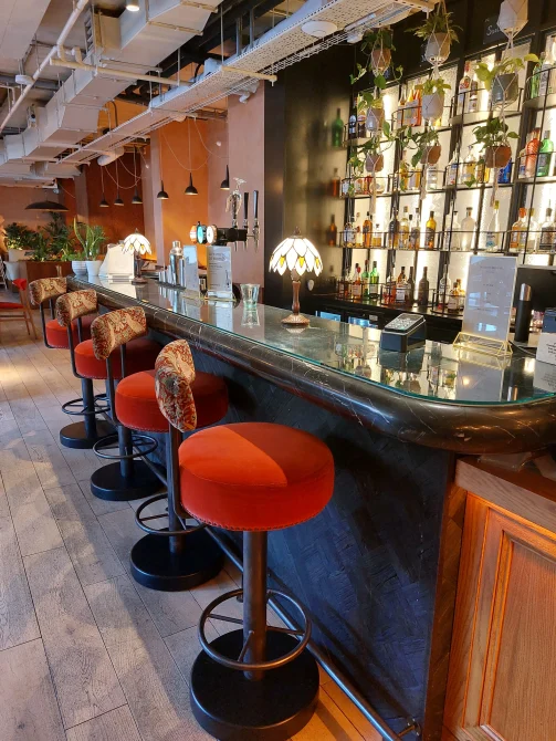 Winnie's bar and cafe at room2 Chiswick hometel in London with red bar stools, curved counter, botanical displays, and craft cocktail selection
