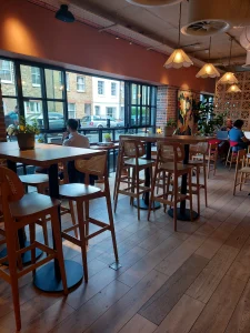 room2 Chiswick lounge and café area with high tables and stools, large street-facing windows, warm pendant lights, and guests working on laptops