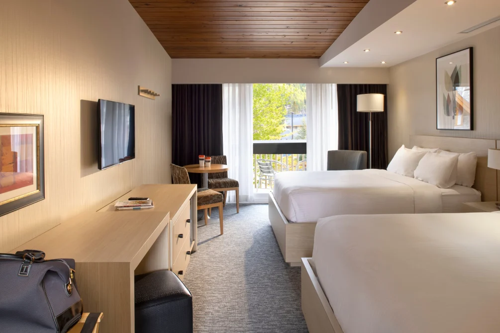 Premium room with two queen beds at Banff Aspen Lodge featuring spacious layout, private balcony, work desk, flat-screen TV, and warm wood ceiling in Banff, Alberta