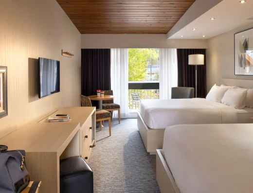 Premium room with two queen beds at Banff Aspen Lodge featuring spacious layout, private balcony, work desk, flat-screen TV, and warm wood ceiling in Banff, Alberta