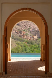 Arched doorway framing view of Berber village nestled in Atlas Mountains with pool and traditional architecture at Kasbah du Toubkal