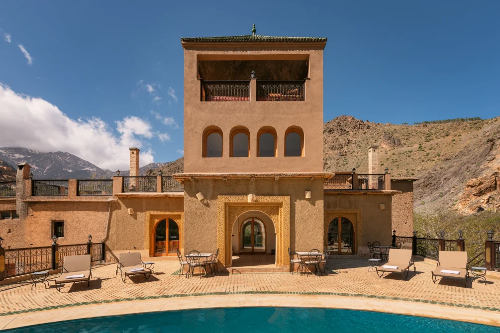 Kasbah du Toubkal courtyard with traditional Moroccan architecture, pool, lounge chairs, and Atlas Mountains backdrop