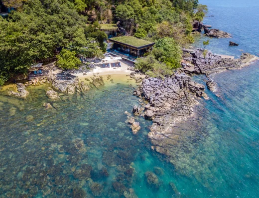 Aerial view of The Beach Retreat nestled on a rocky cove with pristine turquoise waters, sandy beach, and lush jungle canopy.