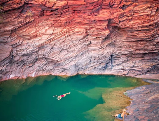 Swimmers in an emerald gorge pool beneath layered red rock walls in Karijini National Park near Karijini Eco Retreat