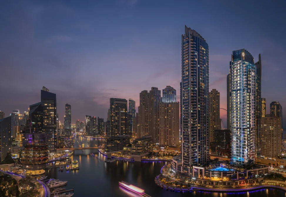 InterContinental Dubai Marina hotel at dusk with illuminated high-rise towers overlooking the marina waterway, surrounded by Dubai skyline and waterfront promenade