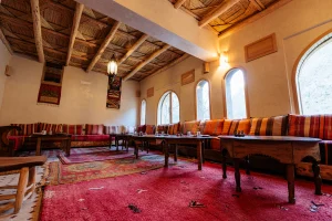 Traditional Moroccan lounge with Berber rugs, low wooden tables, striped cushions, arched windows, and woven ceiling at Kasbah du Toubkal