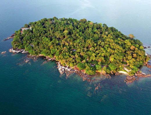 Aerial view of Krabey Island surrounded by turquoise waters, with dense jungle canopy and rocky shoreline visible from above.
