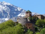 Kasbah du Toubkal with green-roofed tower perched above trees with snow-capped Atlas Mountains behind