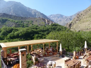 Rooftop terrace at Kasbah du Toubkal with pergola lounge seating, dining tables, and panoramic Atlas Mountains valley view