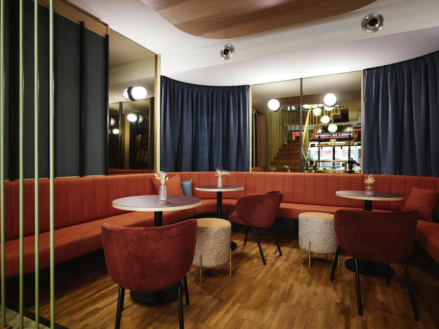 Modern lounge at Hotel Henriette Vienna with coral banquette seating, round tables, contemporary lighting, and mirrored walls creating an intimate gathering space