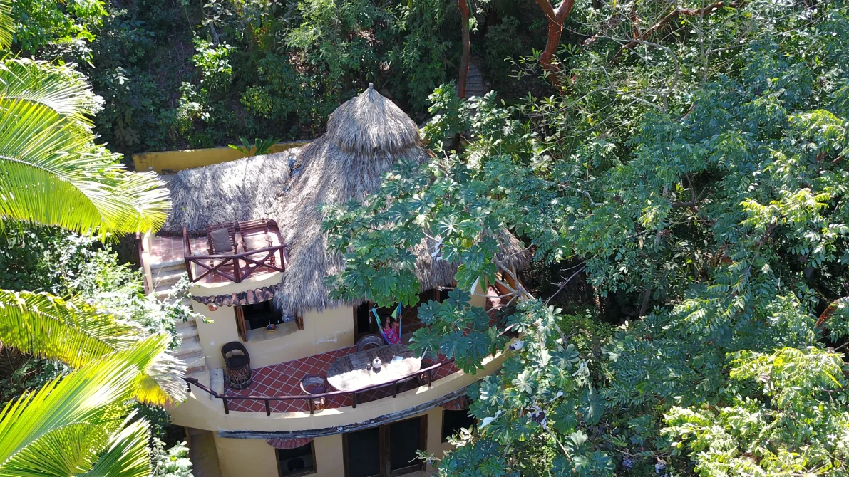 Aerial view of thatched-roof casita with multiple decks at Tailwind Jungle Lodge in San Pancho, Nayarit Mexico, surrounded by dense tropical rainforest canopy