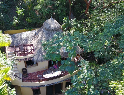 Aerial view of thatched-roof casita with multiple decks at Tailwind Jungle Lodge in San Pancho, Nayarit Mexico, surrounded by dense tropical rainforest canopy