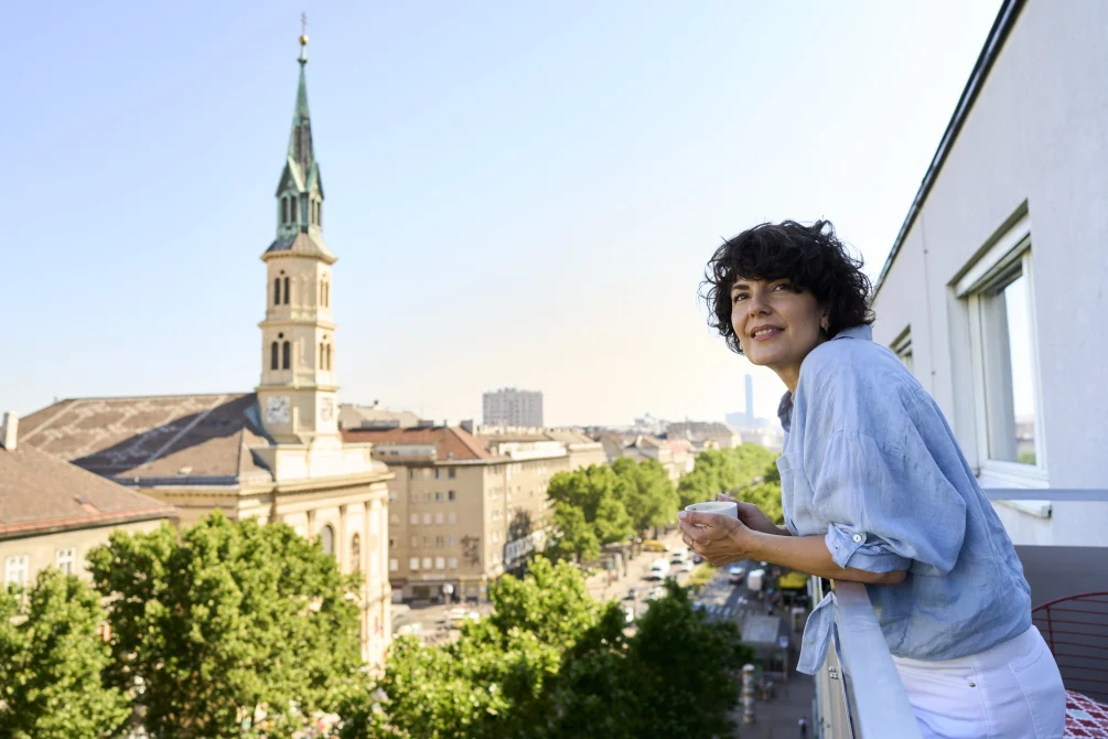 Guest on a balcony at Hotel Henriette in Vienna, Austria, overlooking leafy streets and a historic church tower in the city skyline