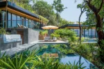 A private pool at The Beach Retreat with modern glass-fronted villas, sun loungers under an umbrella, and lush tropical landscaping.