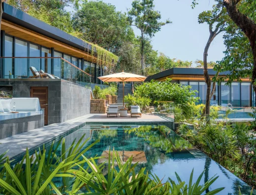 A private pool at The Beach Retreat with modern glass-fronted villas, sun loungers under an umbrella, and lush tropical landscaping.