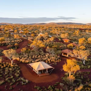 Aerial view of Karijini Eco Retreat with safari tents and cabins scattered across red outback landscape and native bush at sunset