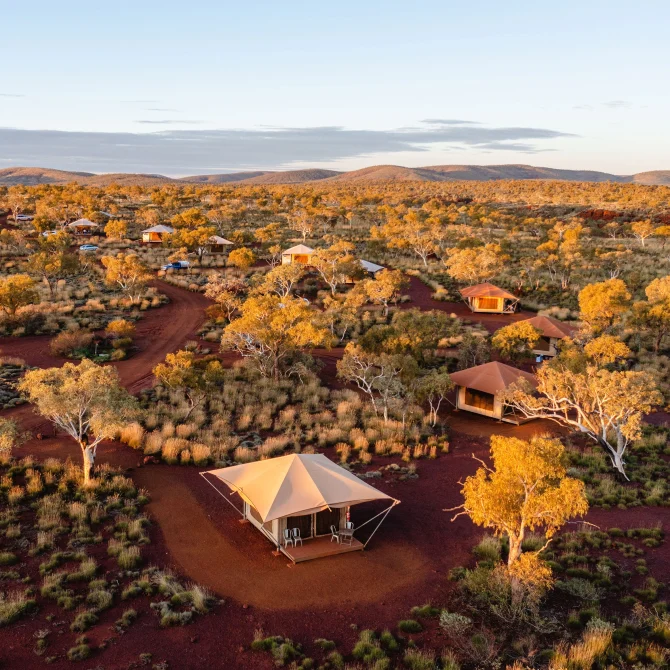 Aerial view of Karijini Eco Retreat with safari tents and cabins scattered across red outback landscape and native bush at sunset