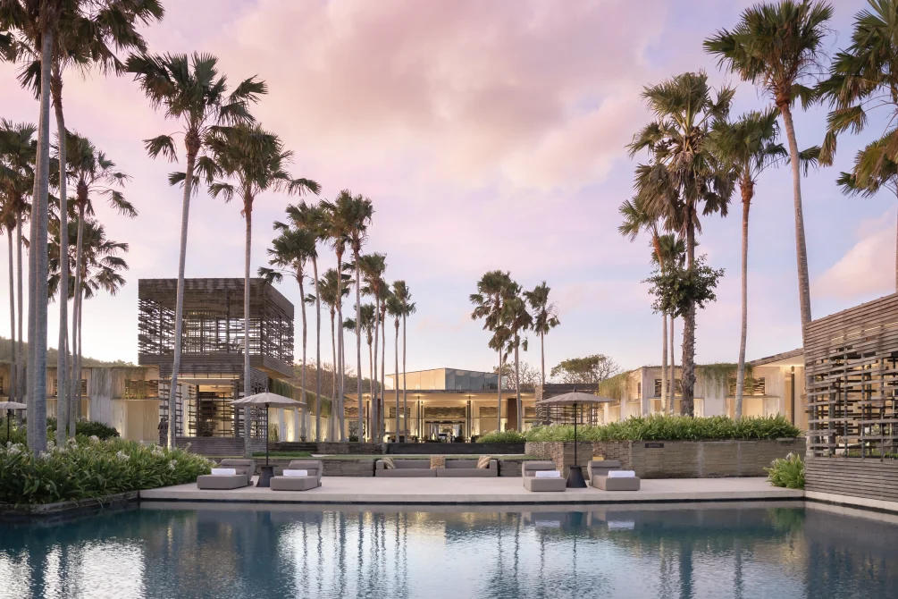 Morning view of Alila Villas Uluwatu with infinity pool, palm trees, modern architecture, and lounge beds under a pastel sky