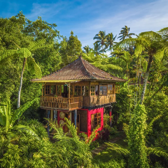 Aerial view of a traditional Balinese bungalow with red accents and tiled roof surrounded by lush tropical forest at Sarinbuana Eco Lodge