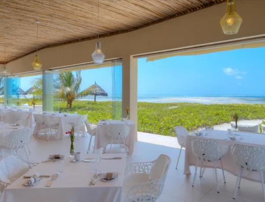 Beachfront restaurant dining area with white table settings, modern chairs, and panoramic ocean views at White Sand Villas