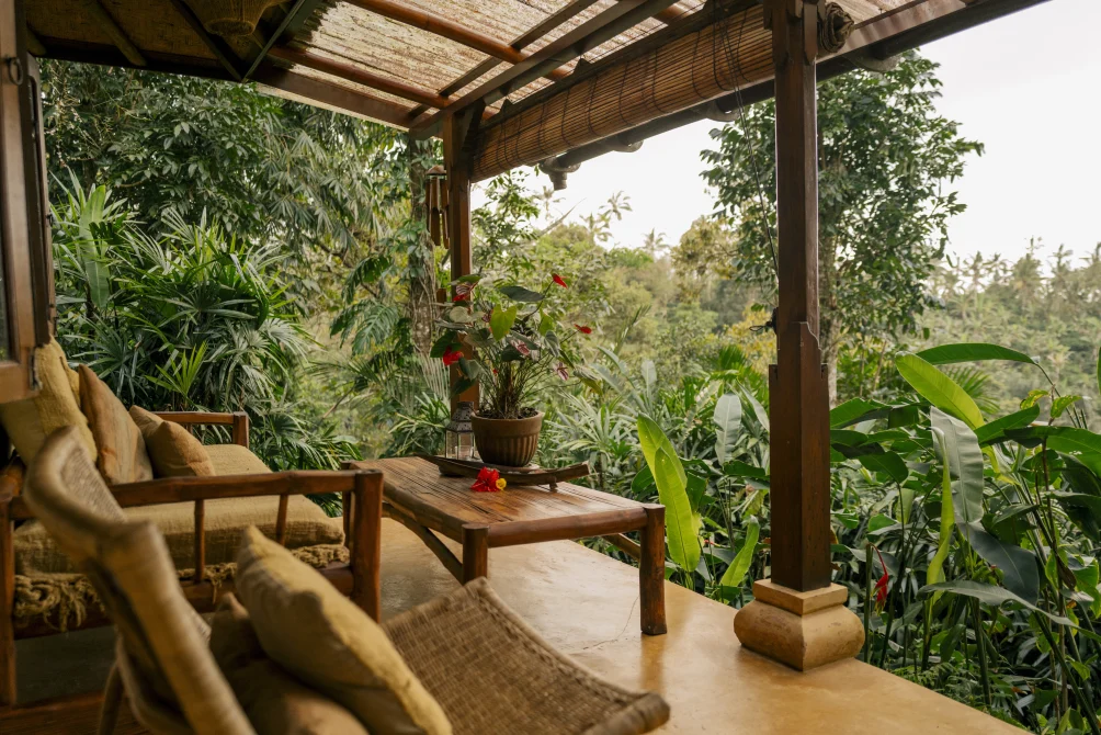 Covered terrace with seating and a wooden table overlooking tropical greenery at Sarinbuana Eco lodge, Bali.