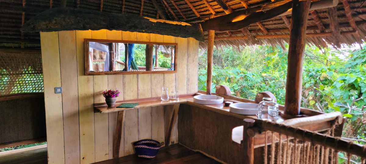 Open-air tree house bathroom with double white sinks, wooden counter, and thatched roof overlooking lush greenery at Chole Mjini
