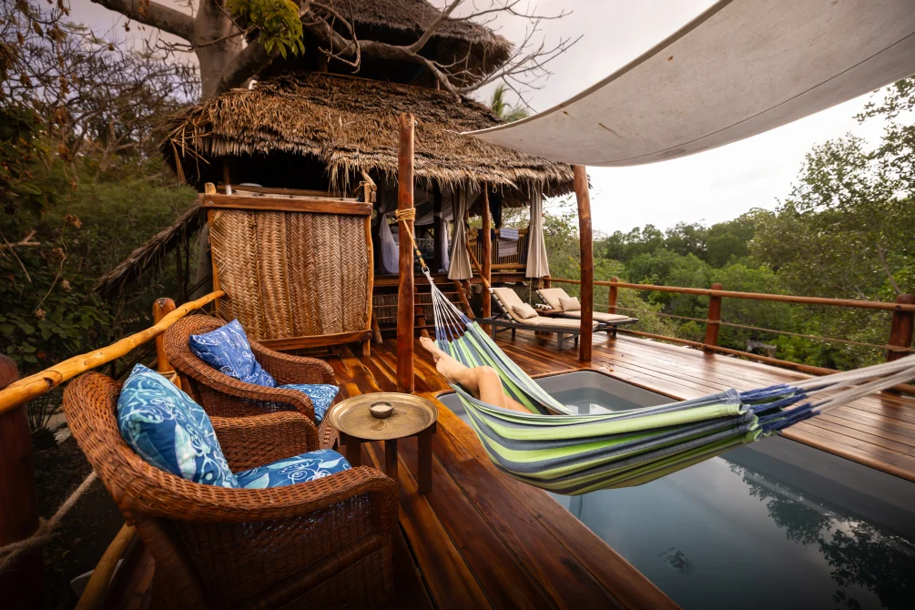 Tree house deck with woven rattan chairs, colorful hammocks, and infinity pool overlooking forest canopy at Chole Mjini