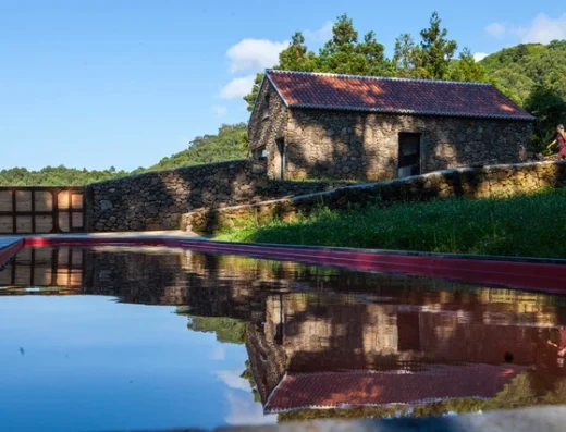 Historic stone building reflected in still water with forest backdrop and red wooden walkway