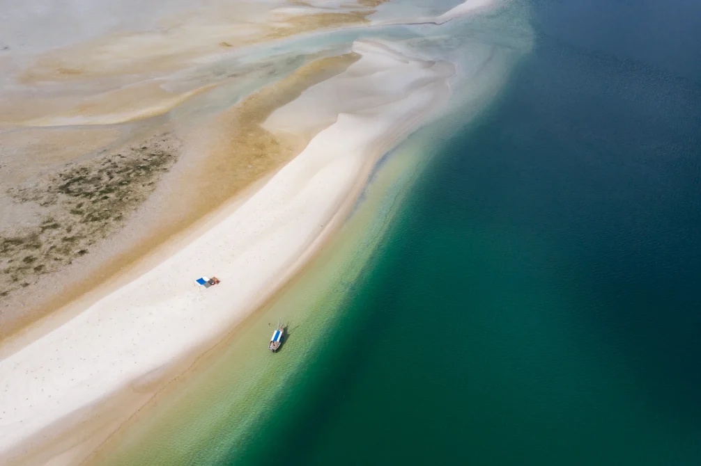 Aerial view of a white sandbank with shallow turquoise lagoon and a small boat anchored offshore during a sandbank excursion near Chole Mjini"
