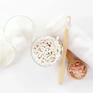 Bamboo cotton buds in a glass bowl with bamboo toothbrush and Himalayan salt on white background