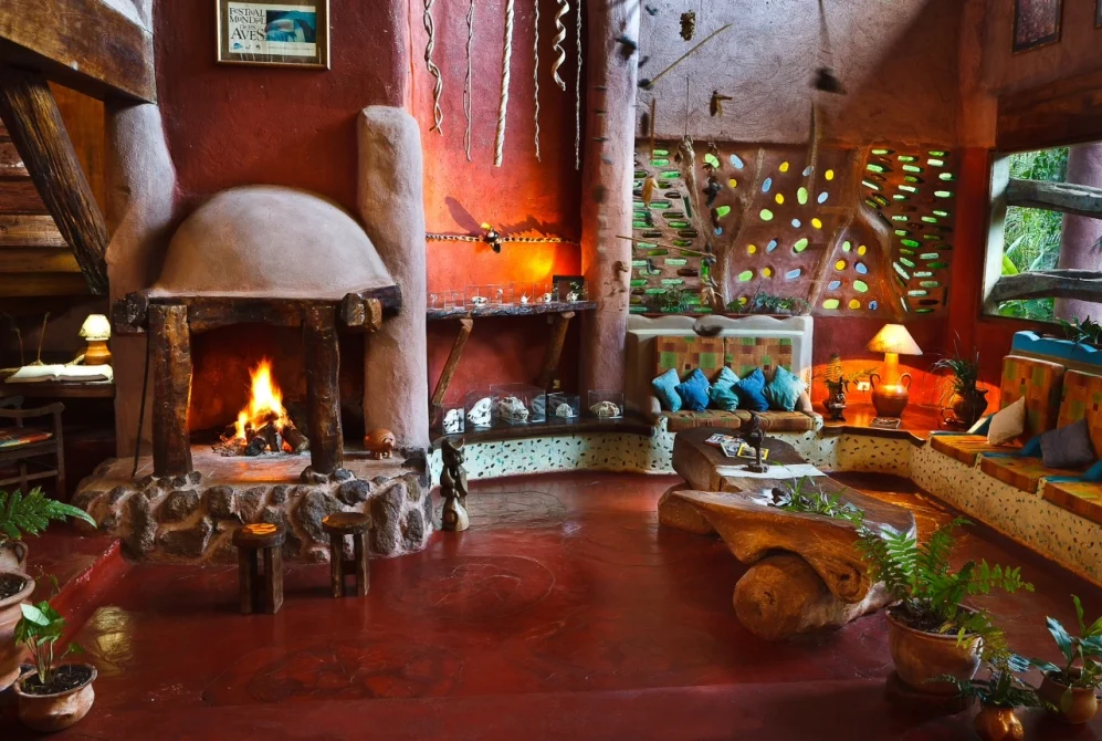 A cozy lodge lobby with a rustic fireplace, organic terracotta walls, colorful seating, and decorative glass panels at Yacutinga Lodge in the rainforest.