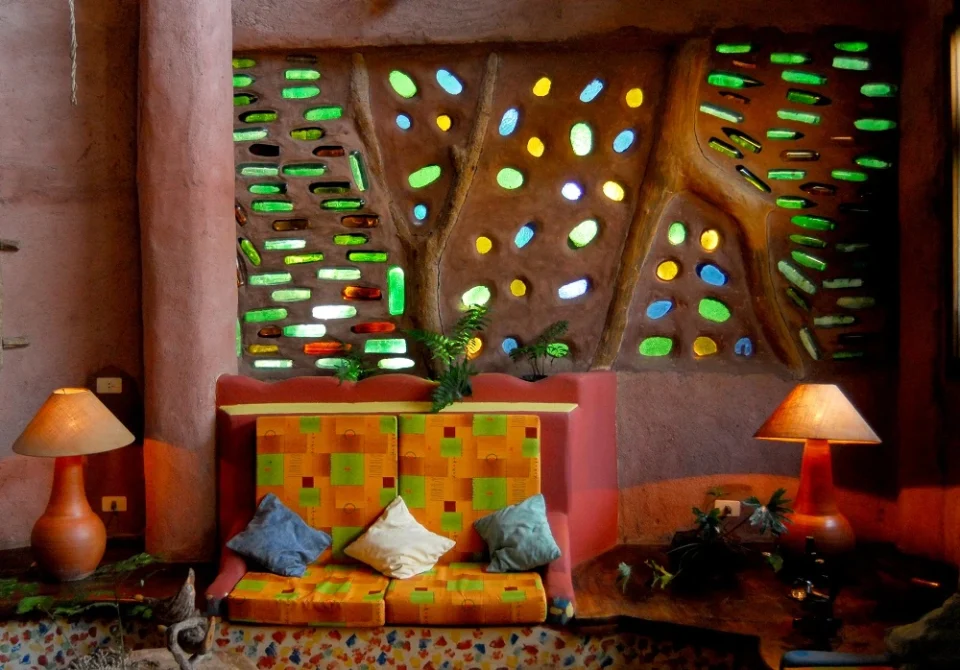 A colorful lounge area with organic architecture featuring decorative glass panels, warm terracotta walls, and handcrafted furnishings at Yacutinga Lodge.