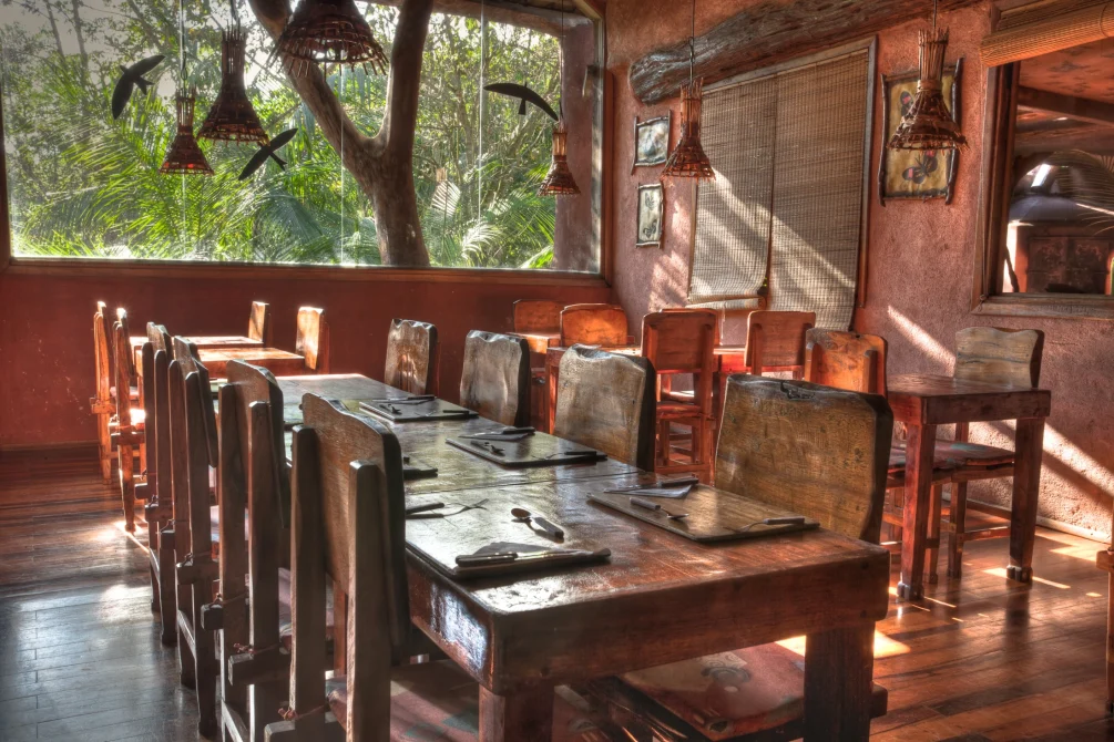 Rustic jungle lodge restaurant with wooden tables and chairs, warm woven pendant lights, and large windows overlooking rainforest greenery at Yacutinga.