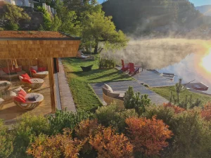 A lakeside spa lounge at Weihrerhof with wooden decking, red loungers, outdoor seating, and morning mist rising from the lake in South Tyrol.