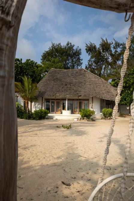 A beachfront bungalow with thatched roof, white walls, wooden deck, and tropical gardens on Zanzibar's white sand beach.