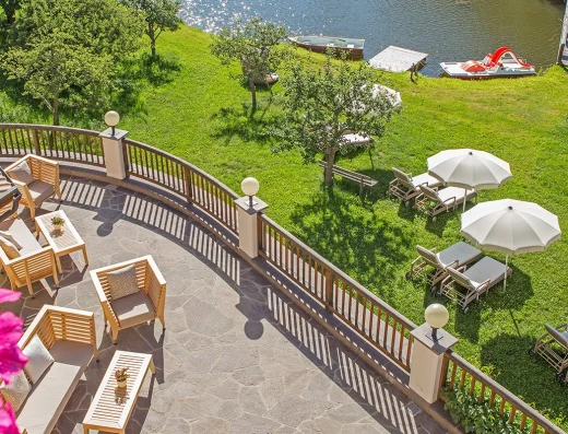 A lakeside terrace at Weihrerhof with wooden loungers, white umbrellas, flowering vines, and boats on the water in summer sunlight.