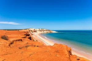 Red cliffs and golden beach coastline in Australia with turquoise ocean and clear blue sky