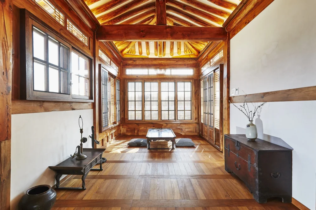 A traditional Korean anbang bedroom with wooden beams, latticed windows, ondol heated floors, and minimal furnishings bathed in warm natural light.