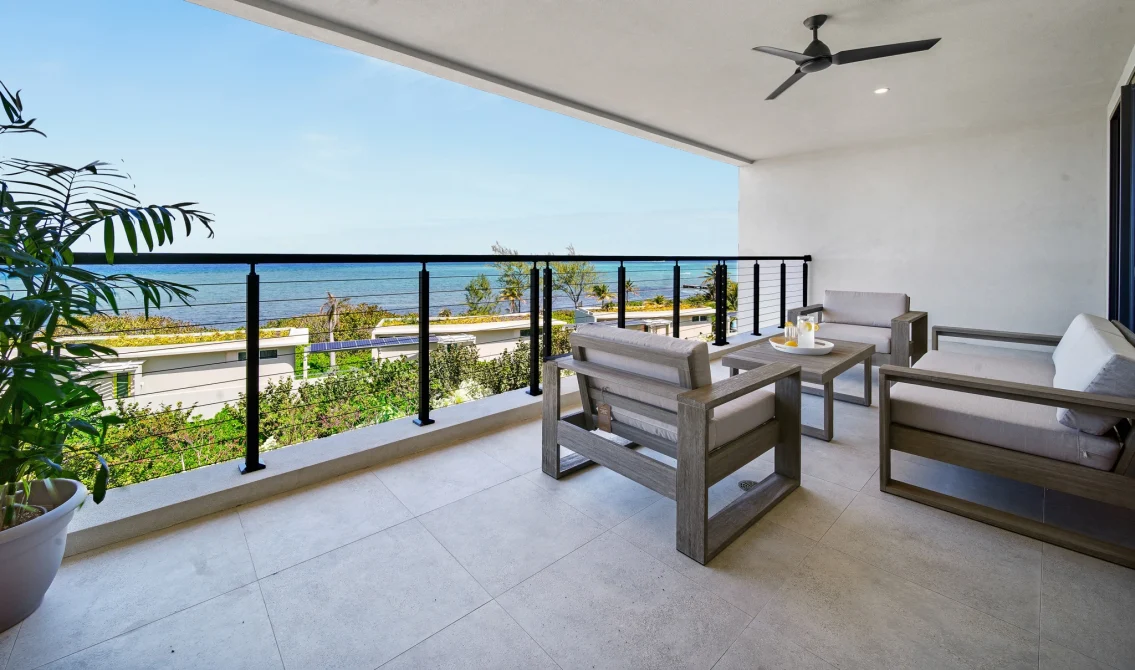 A spacious sea-view balcony at Vida Cayman with modern outdoor lounge seating, ceiling fan, and panoramic Caribbean ocean views.