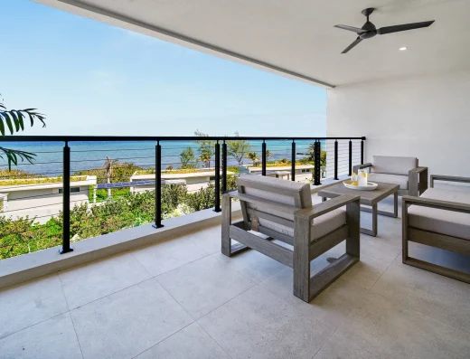 A spacious sea-view balcony at Vida Cayman with modern outdoor lounge seating, ceiling fan, and panoramic Caribbean ocean views.