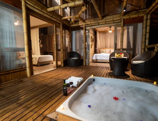 A spacious bamboo suite with an outdoor soaking tub, wooden deck, lounge chairs, and multiple bedroom areas visible through glass doors.