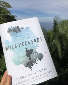 Wildpreneurs book cover by Tamara Jacobi held outdoors with tropical greenery in the background
