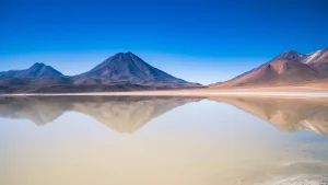 Volcanic peaks reflected in salt lake mirror, high altitude Andes landscape with clear blue sky