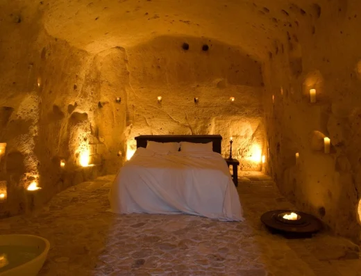 A candlelit cave bedroom carved into golden limestone with a bed, soaking tub, and warm ambient lighting creating an intimate underground sanctuary.