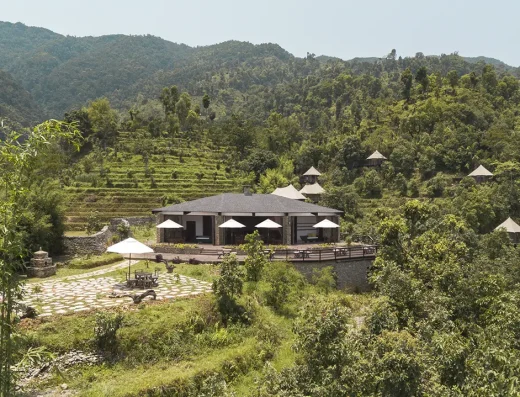 A hillside eco-lodge with a central pavilion and scattered tented cabins surrounded by lush green mountains and terraced fields.