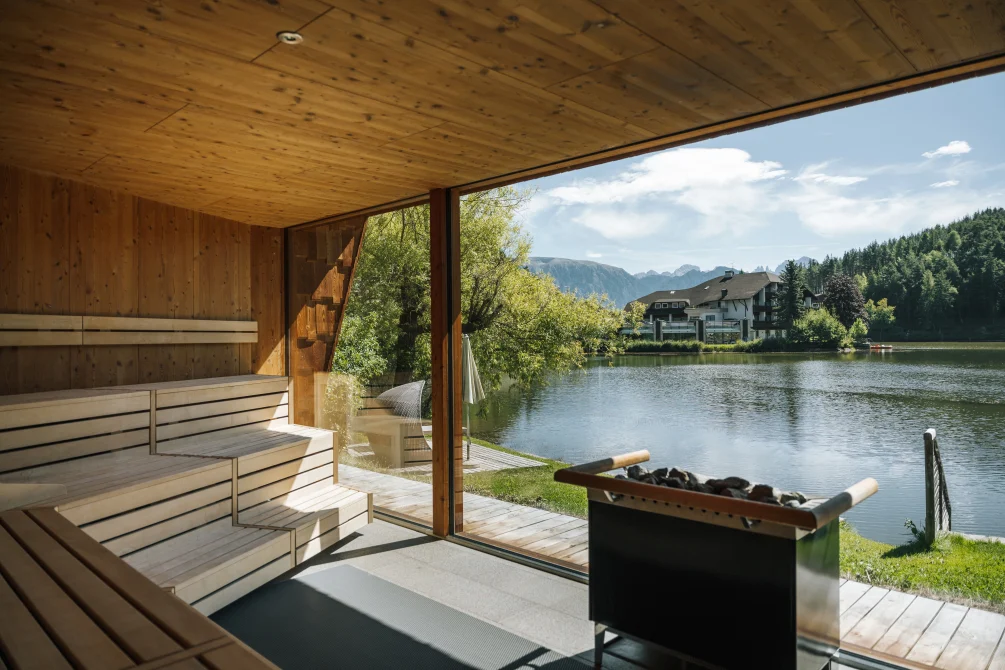 A lakeside sauna with wooden benches and a large window overlooking a calm Alpine lake and mountains at Weihrerhof spa.