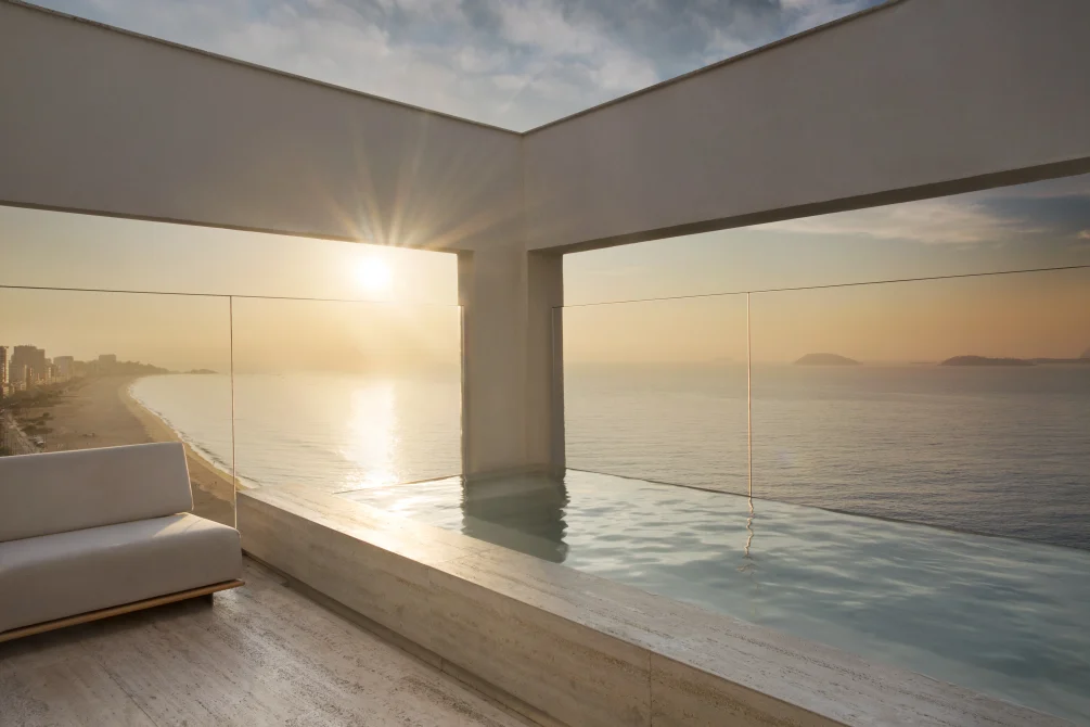 Rooftop infinity pool at sunrise overlooking the ocean and coastline.